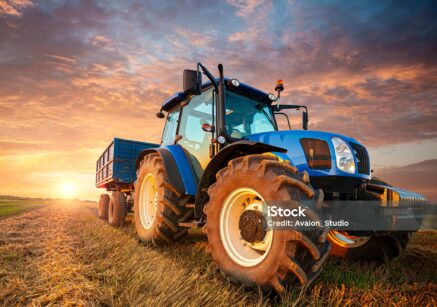 Blue tractor in the field during the harvest. A tractor with a trailer on a stubble field waiting for grain to be loaded.